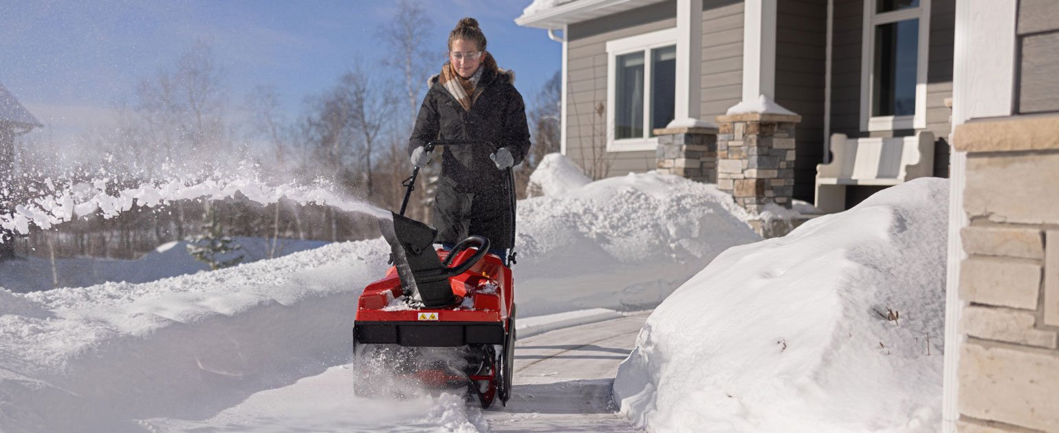 woman using single-stage snow blower on walkway